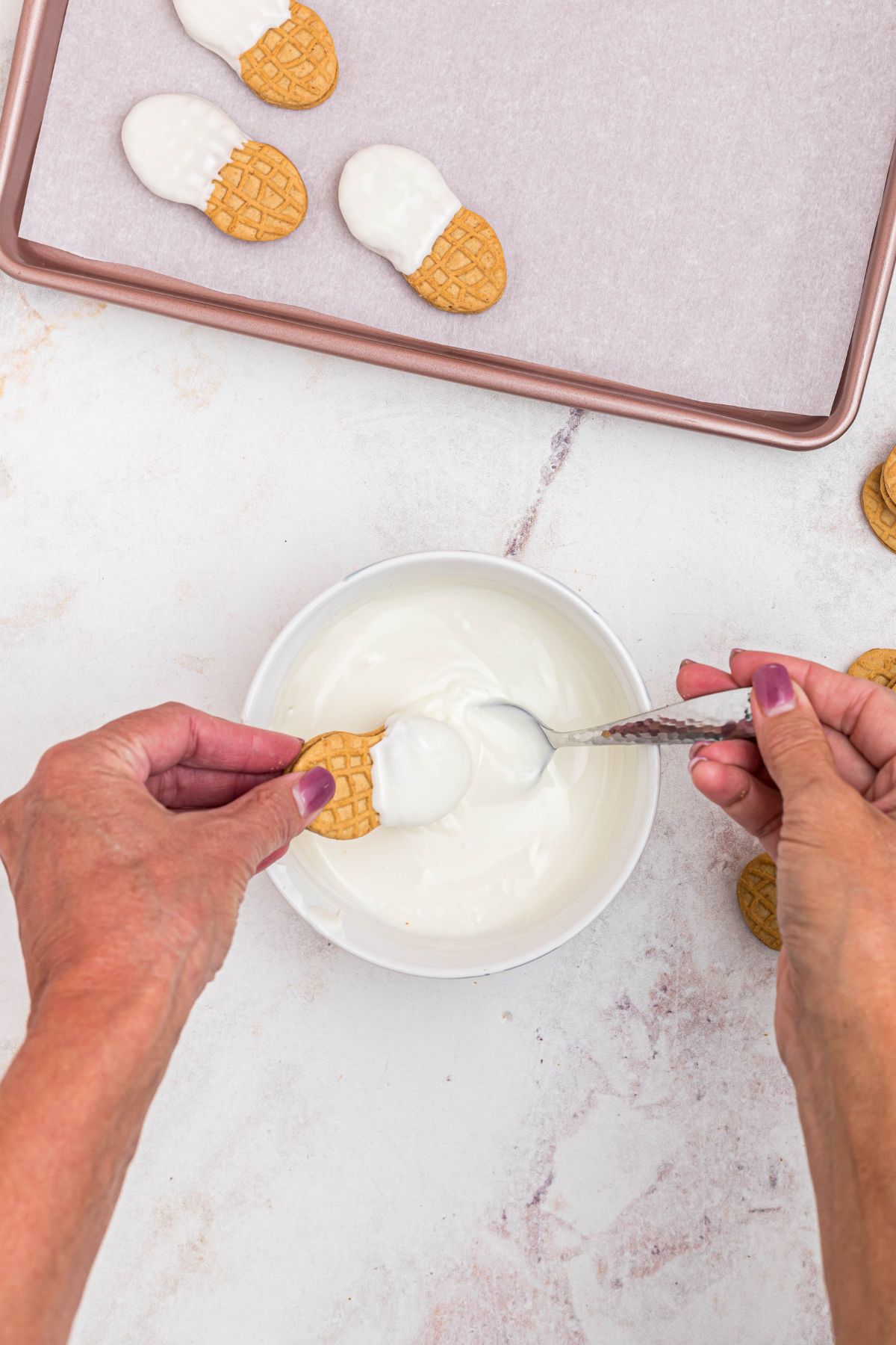 Melted white chocolate in small bowl with peanut butter cookies being dipped halfway. 