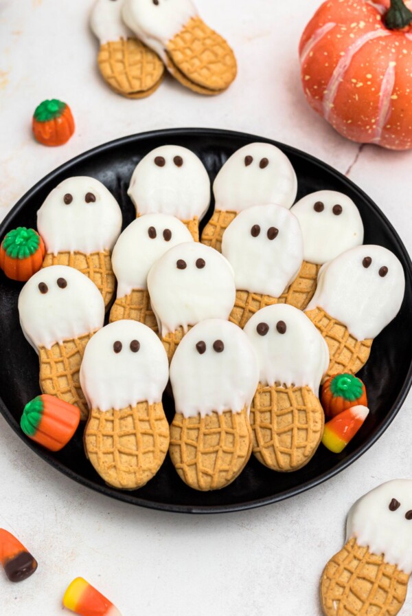 Black plate with peanut butter cookies dipped in white chocolate with chocolate dots for eyes, stacked together, on a marble table.