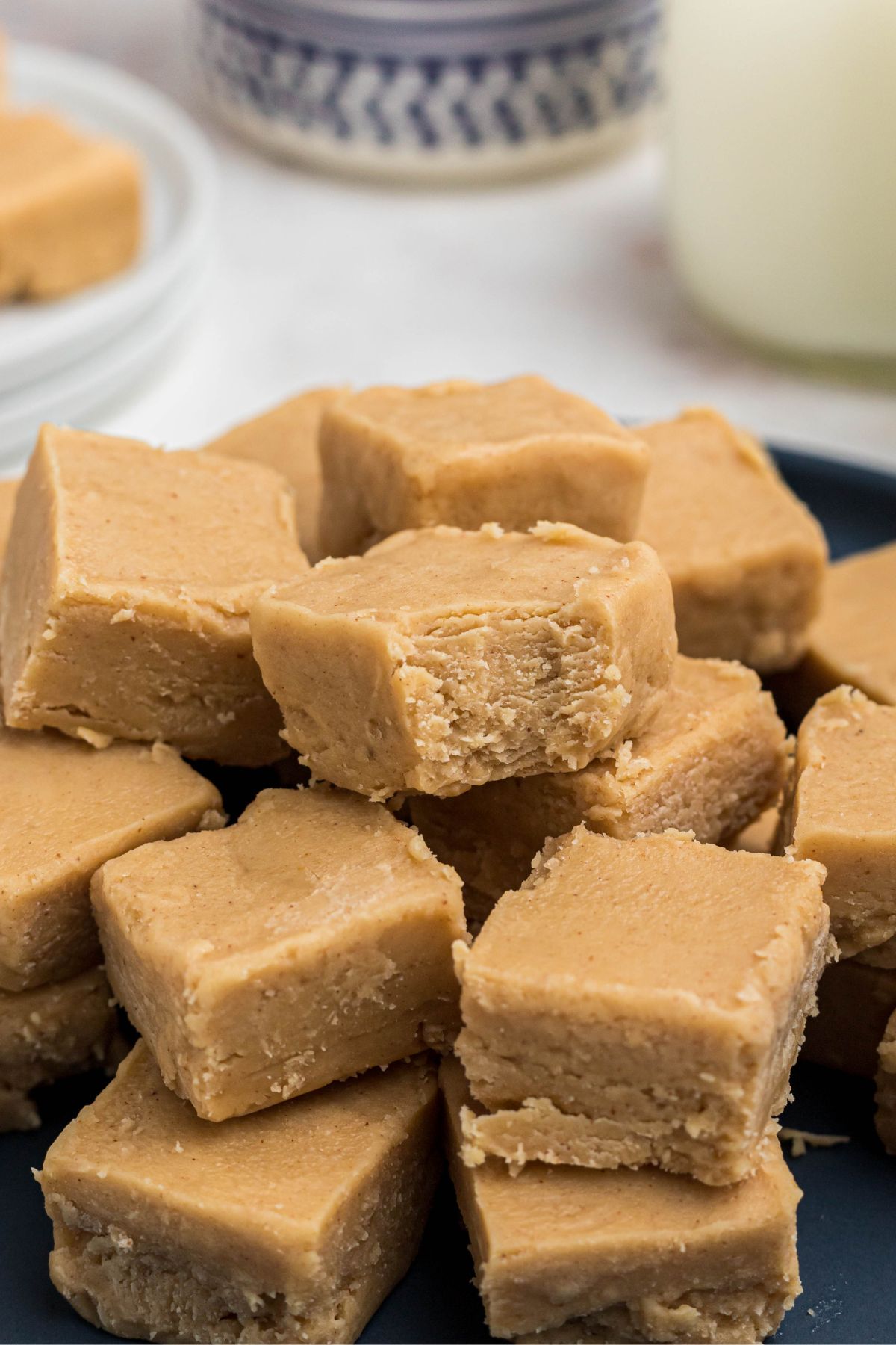 Creamy squares of peanut butter fudge stacked on a blue plate, with the top piece having a bite taken. 