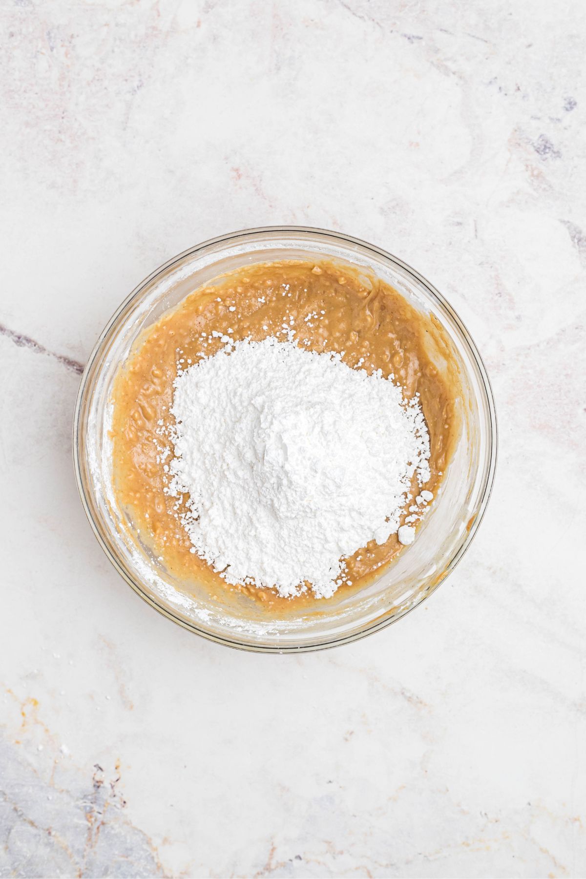 Powdered sugar being mixed with melted butter and peanut butter in a large clear glass bowl. 