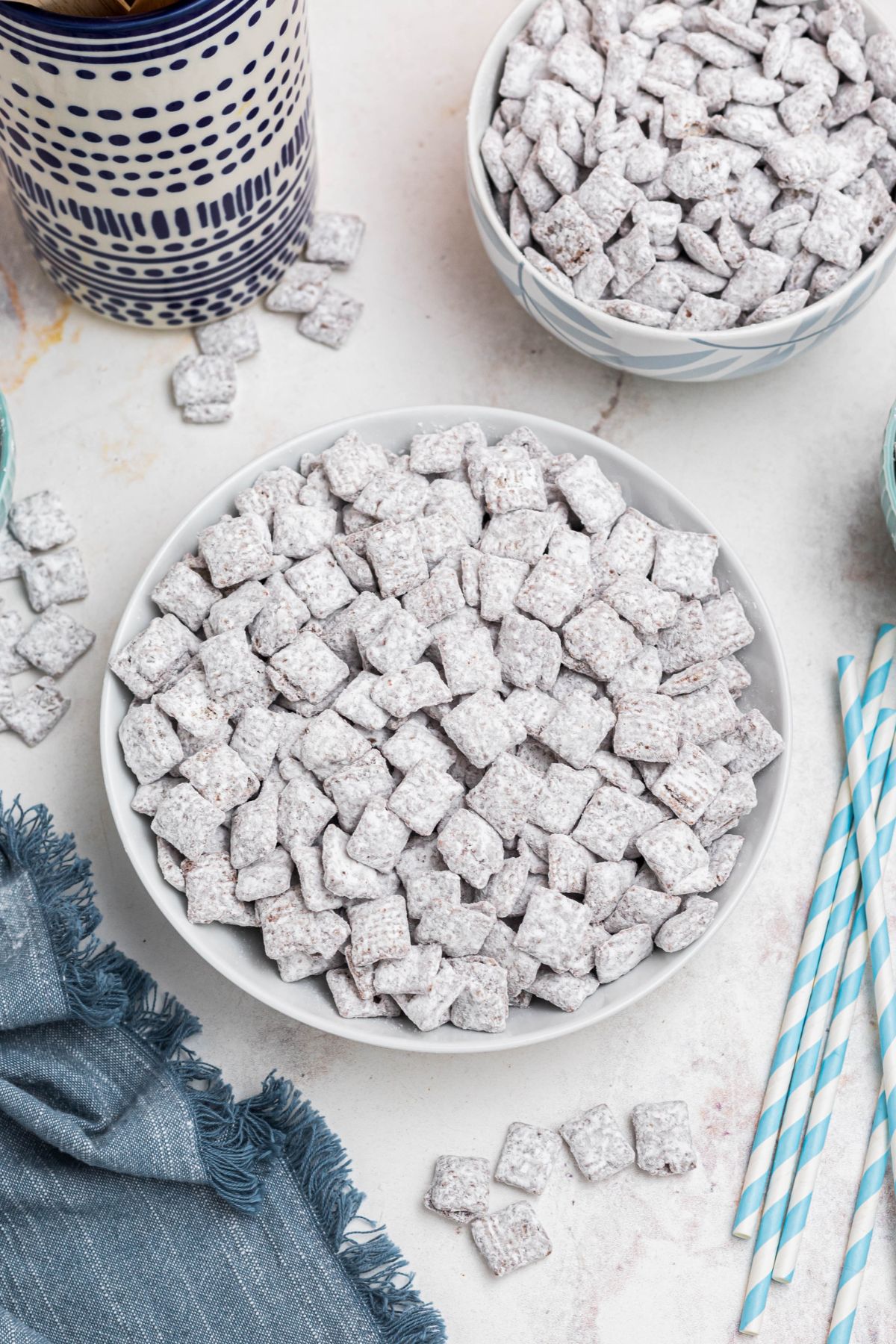 White bowl filled with powdered sugar coated cereal pieces, with blue linen and straws on the table. 
