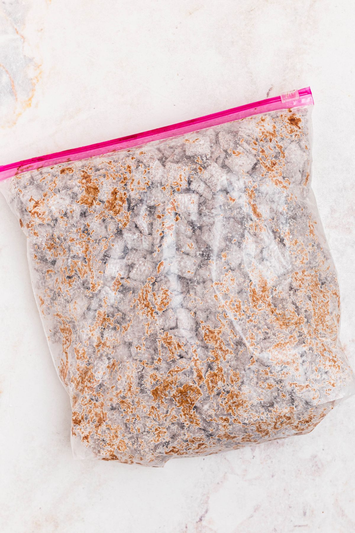 Powdered sugar being mixed in with chocolate coated cereal in a large mixing bag. 
