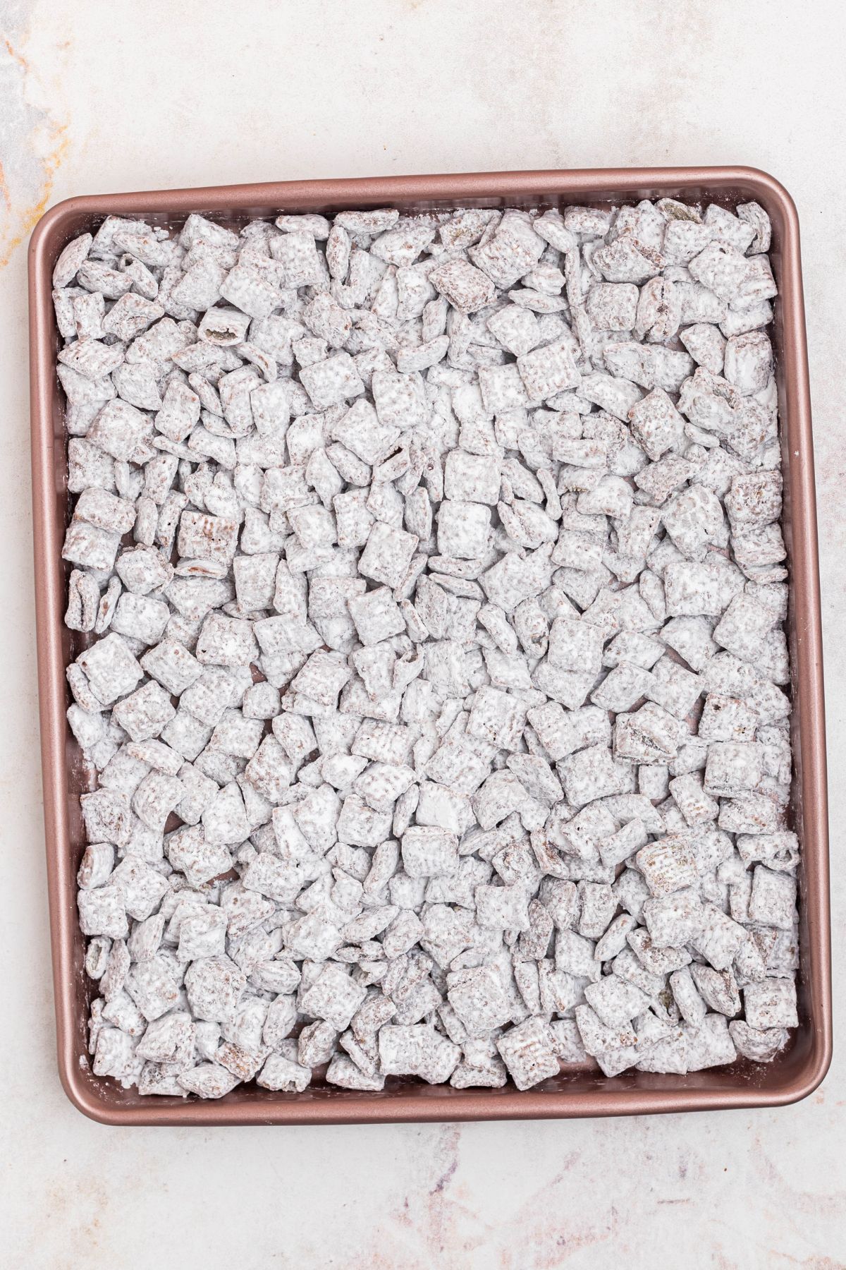 Coated Chex cereal spread out and cooling on a baking sheet. 