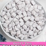 White bowl filled with powdered sugar coated cereal pieces, known as Puppy Chow, with blue linen and straws on the table.