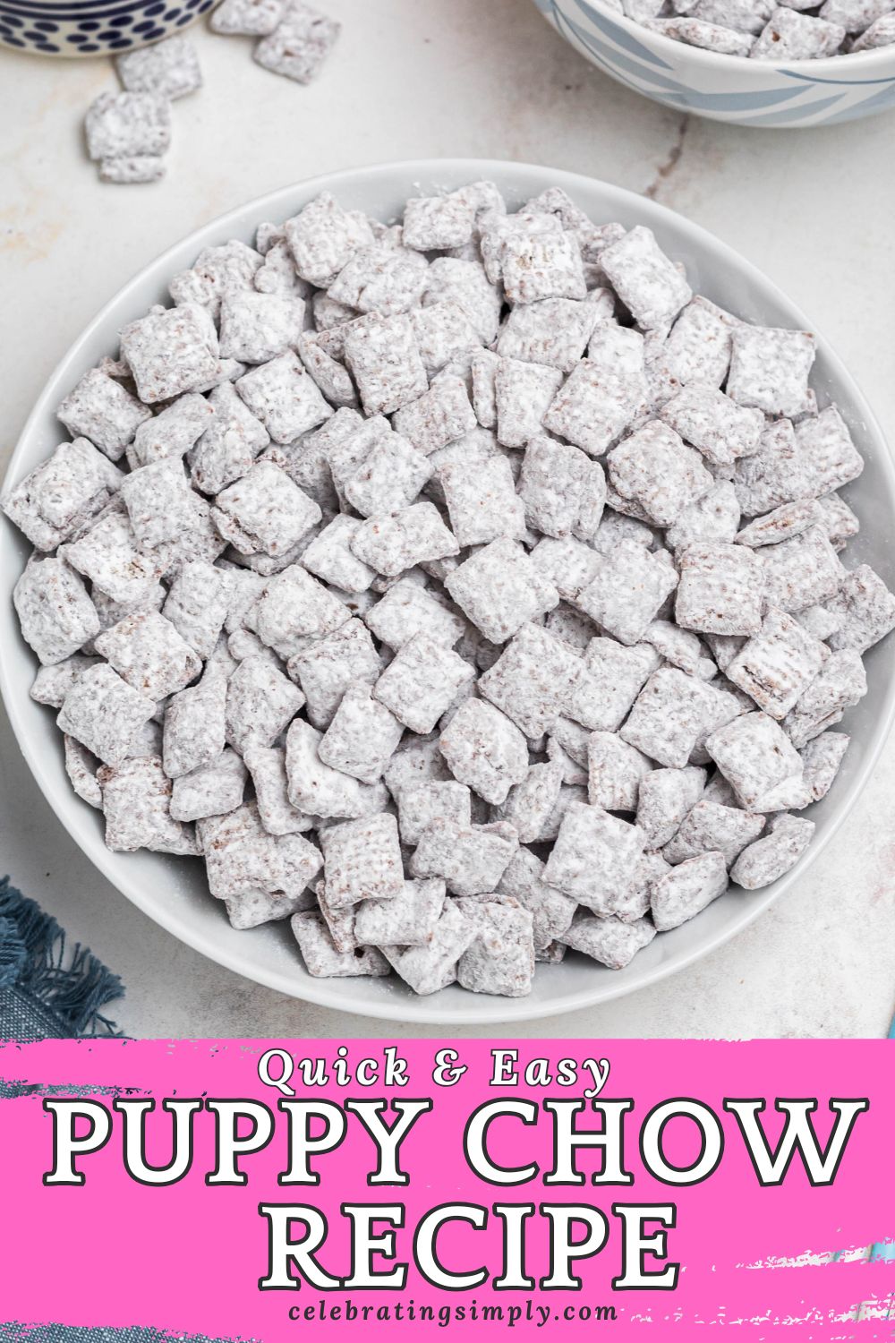 White bowl filled with powdered sugar coated cereal pieces, known as Puppy Chow, with blue linen and straws on the table.