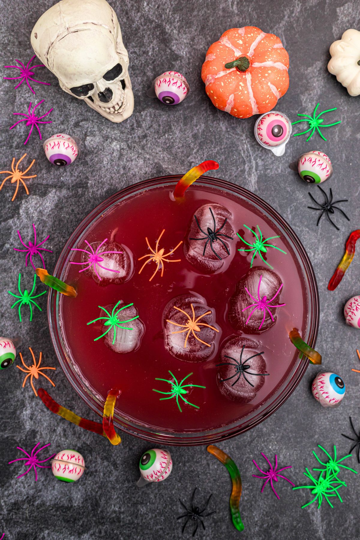 Punch bowl filled with punch and pumpkin shaped ice cubes, and plastic spiders. 