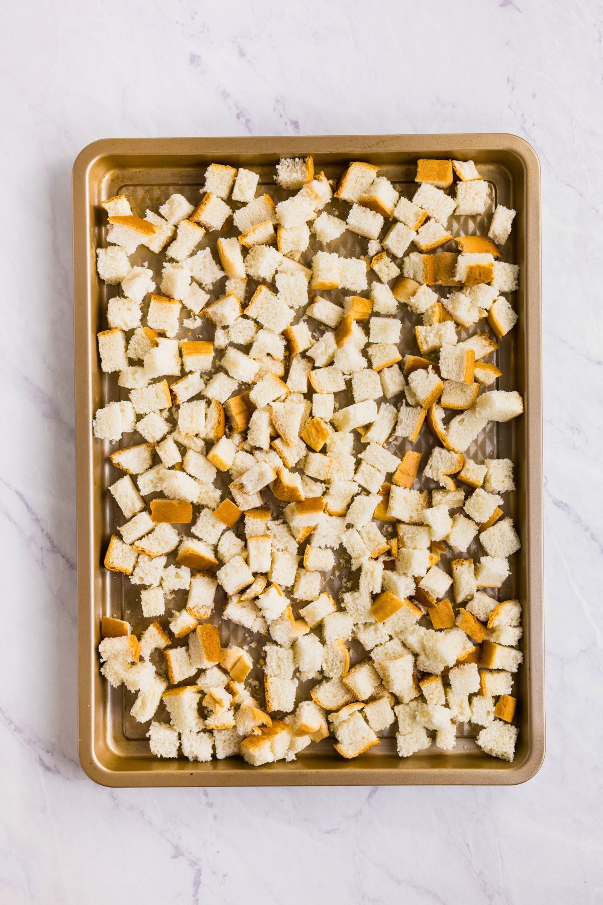 Bread slices cut into one inch cubes, spread out onto a baking sheet.