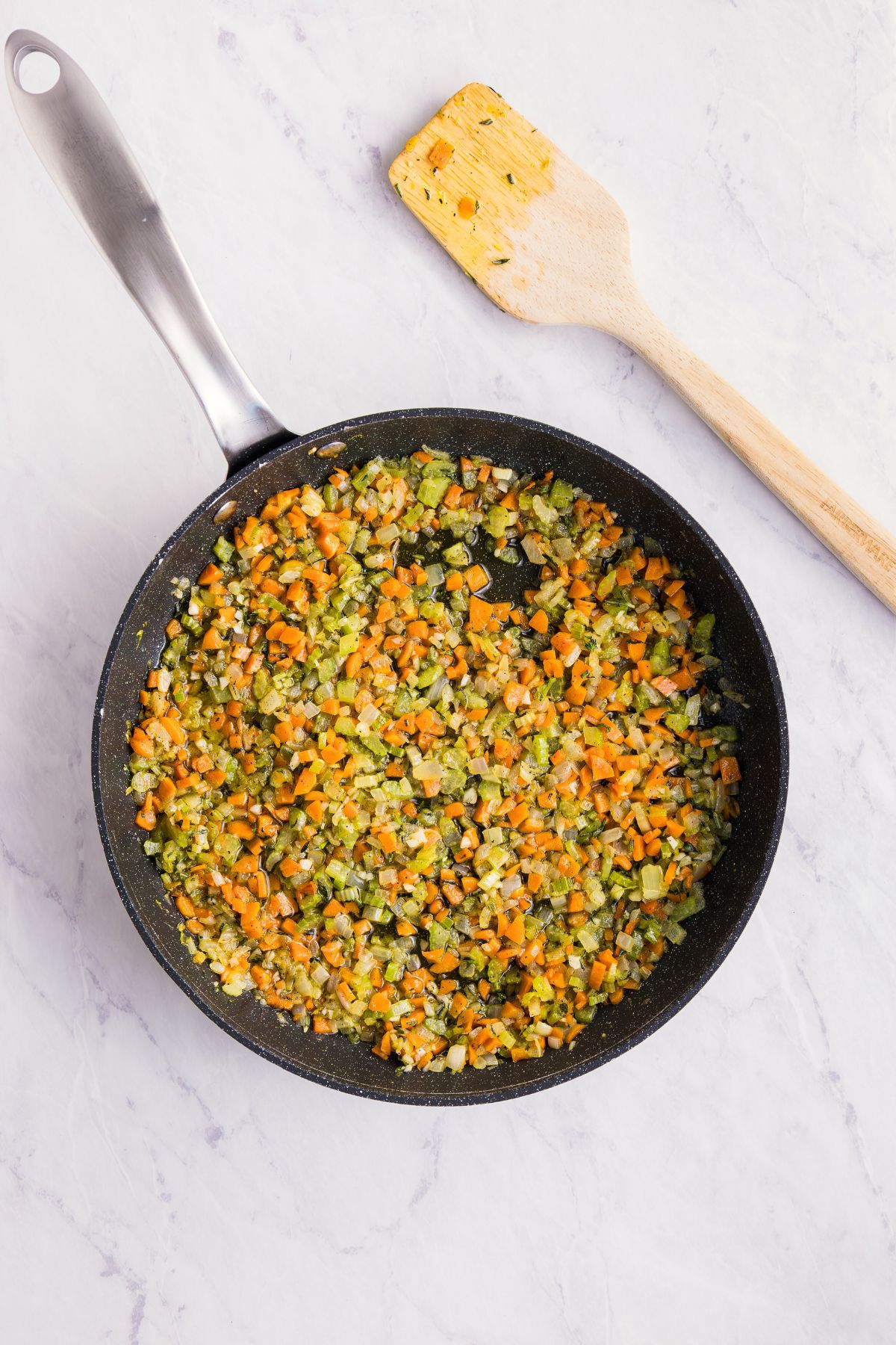 Carrots, celery, onion, and other ingredients, being sautéed in a large skillet.