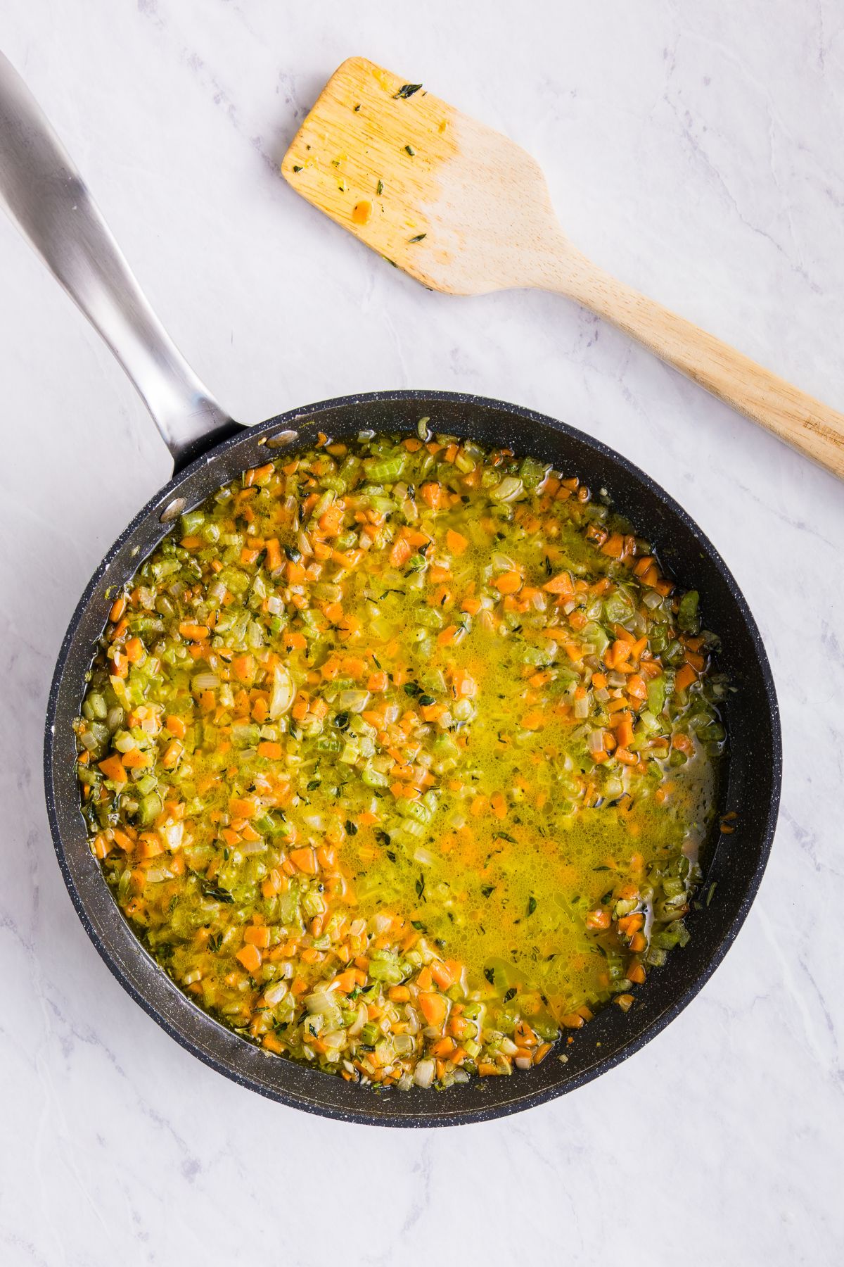 Chicken broth being added to cooked veggies and other ingredients in a skillet.