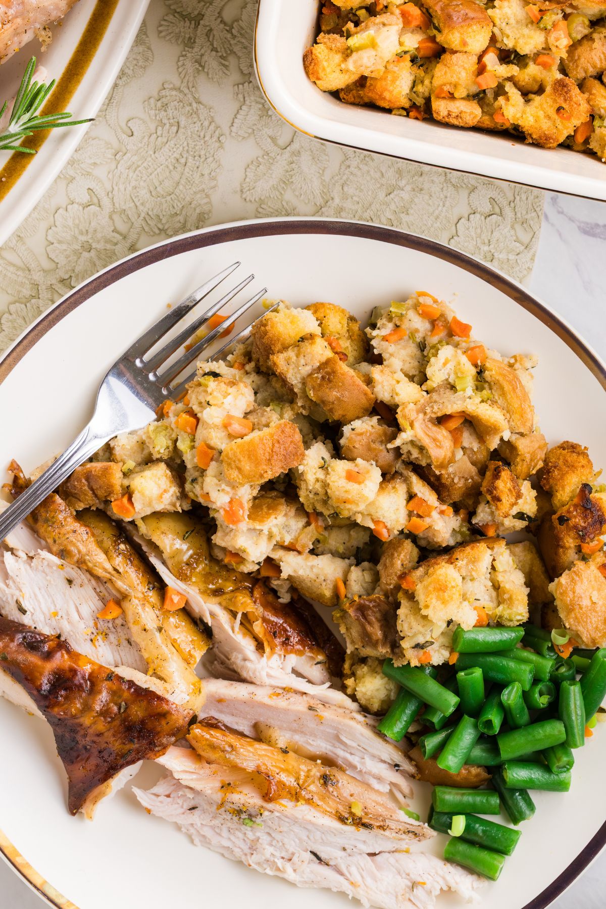 Homemade stuffing served with roasted turkey and green beans on a white dish.