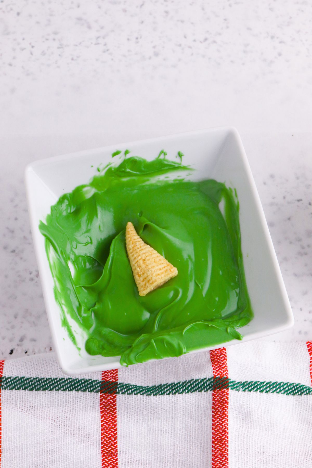 Melted green candy melts in a square dish, with a corn chip bugle being dipped in the center. 