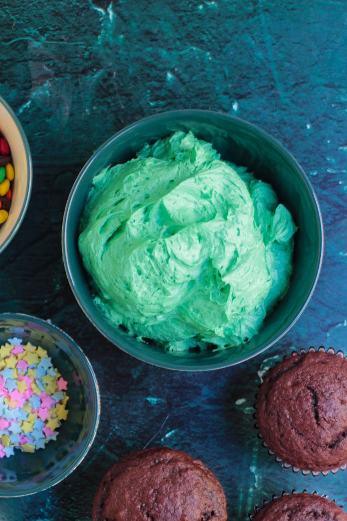 Green buttercream frosting in a clear glass bowl, before using to create trees on cupcakes.