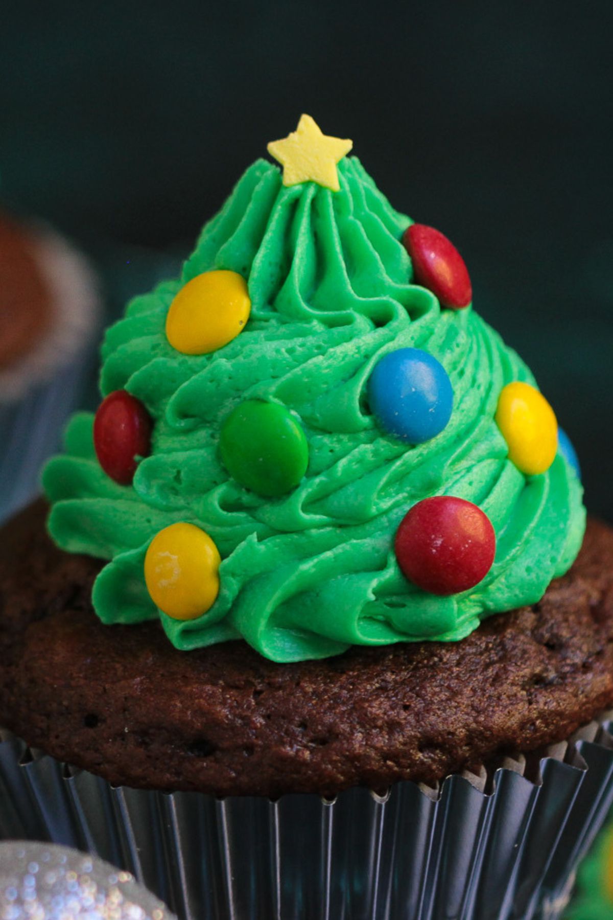 Mini candies pressed into green buttercream to look like lights and ornaments on a tree cupcake.