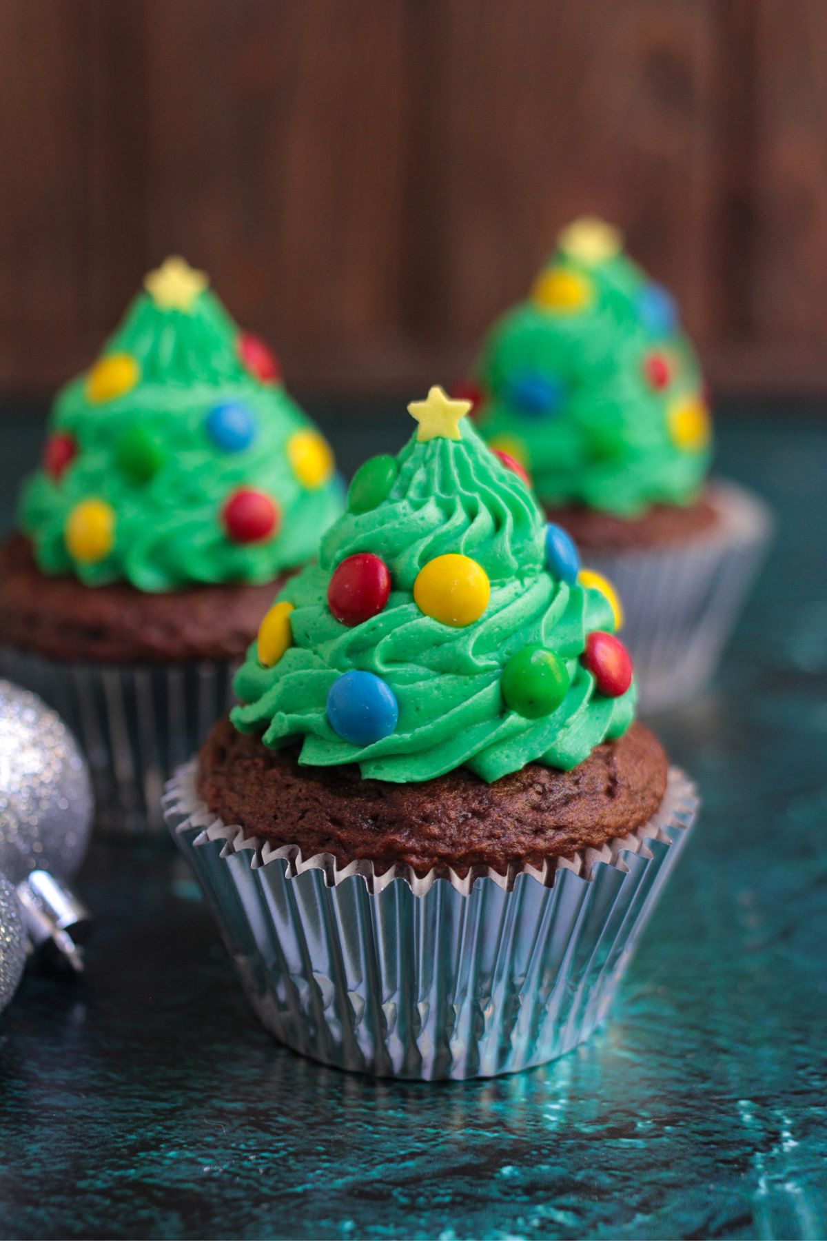 Chocolate cupcakes, frosting with green buttercream swirls in the shape of trees, decorated with mini candies for lights and star sprinkle for topper.