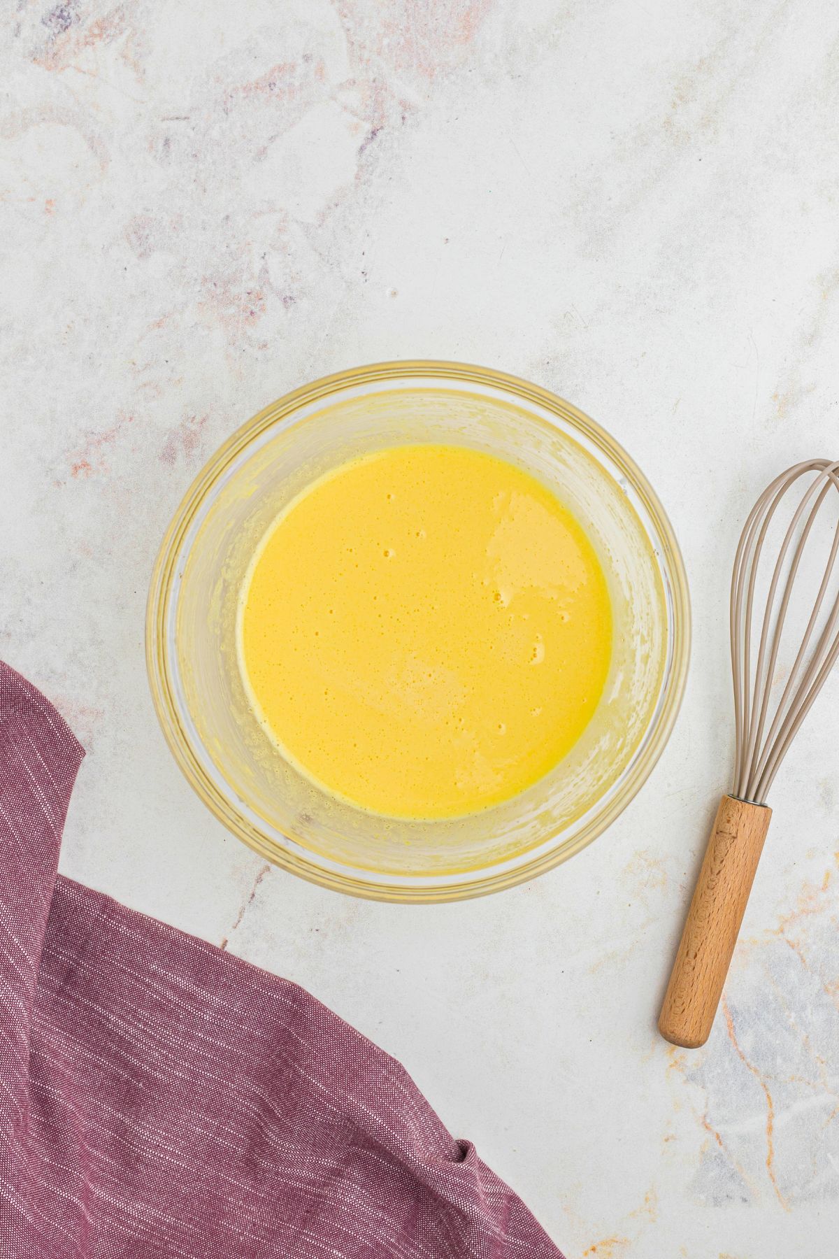Whisked egg yolks with sugar in a clear glass bowl.