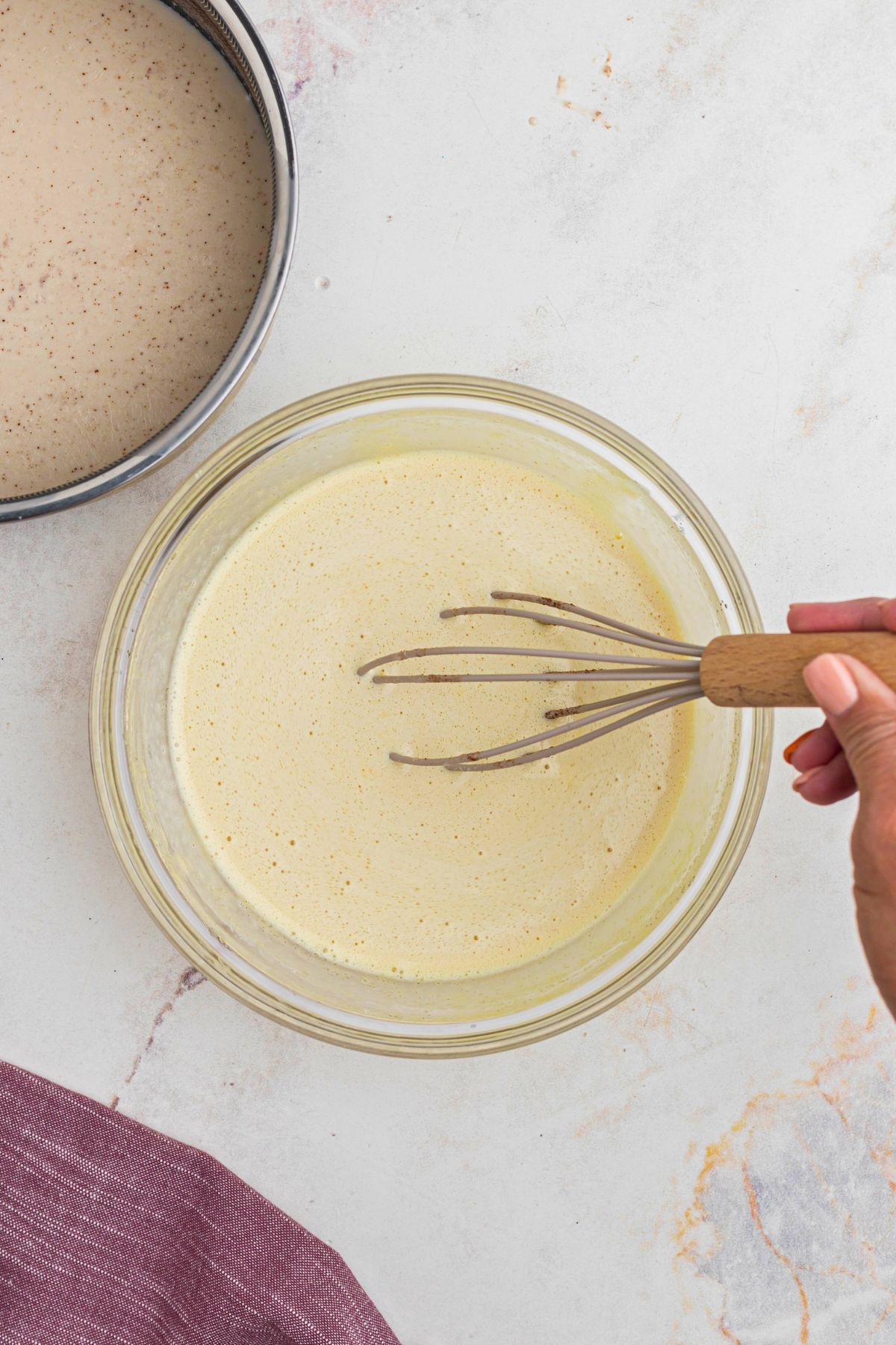 Warmed milk and cream mixture slowly being whisked into egg and sugar mixture.