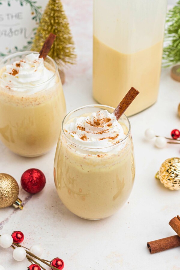 Creamy eggnog in a clear glass, topped with whipped cream and a cinnamon stick.