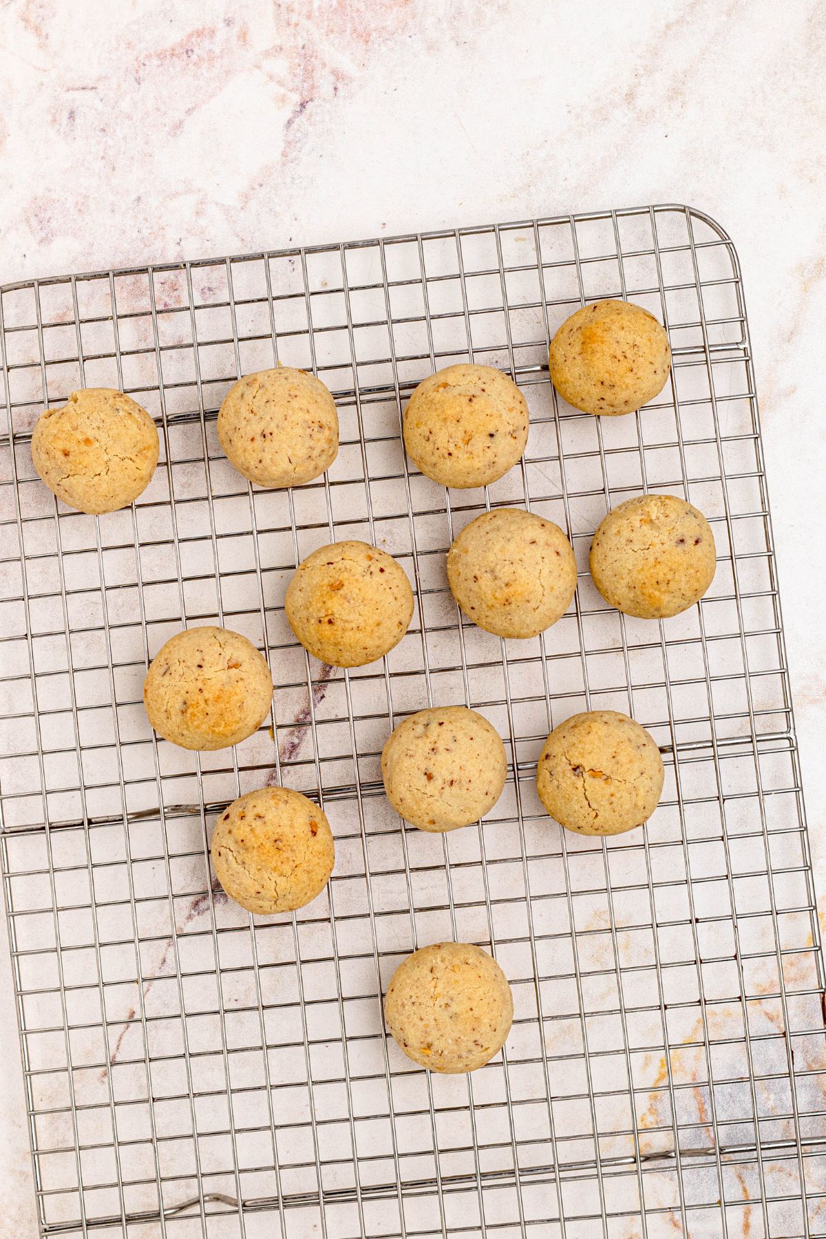 Baked cookies cooling on a wire rack, before dipping into powdered sugar.