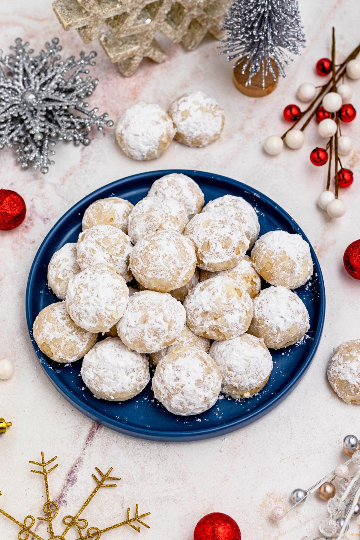 Powder sugar coated Snowball cookies, stacked on a blue plate with holiday party favors on the table around the plate.