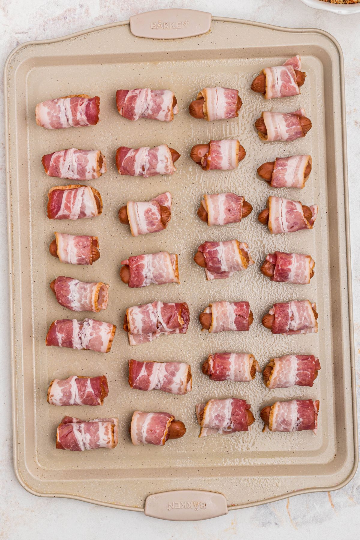 Bacon wrapped smokies on a baking sheet, before being coated in brown sugar and paprika and before being cooked. 