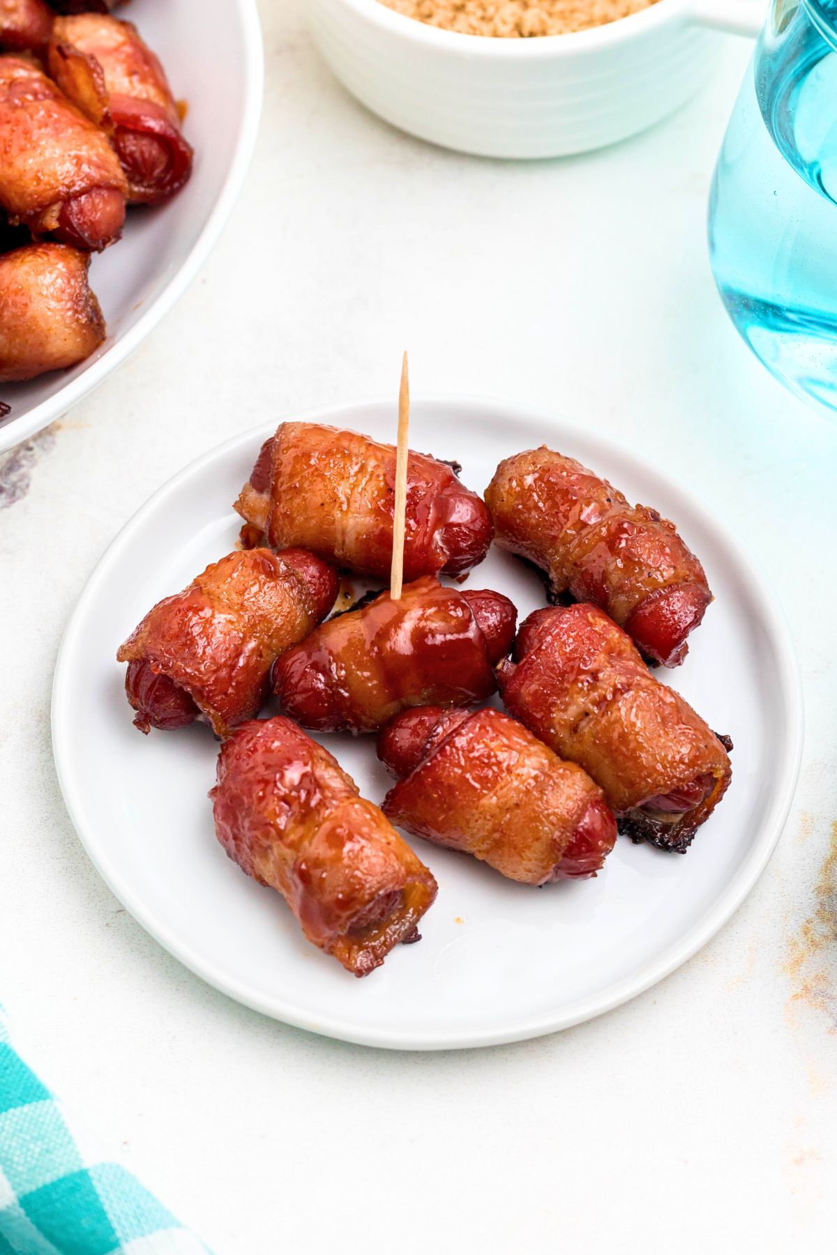 Bacon wrapped smokies on a small white plate with glasses of water on the table.