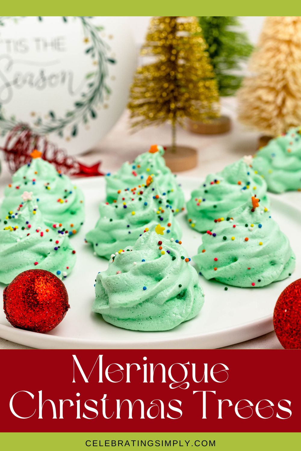 Green meringue trees on a white plate, with Christmas ornaments and mini trees on the table.