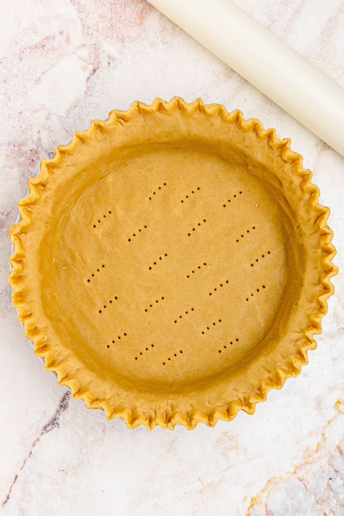 Golden uncooked pie crust in a pie plate, with fluted fork holes. 