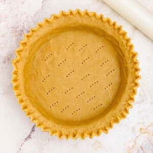 Golden uncooked pie crust in a pie plate, with fluted fork holes.