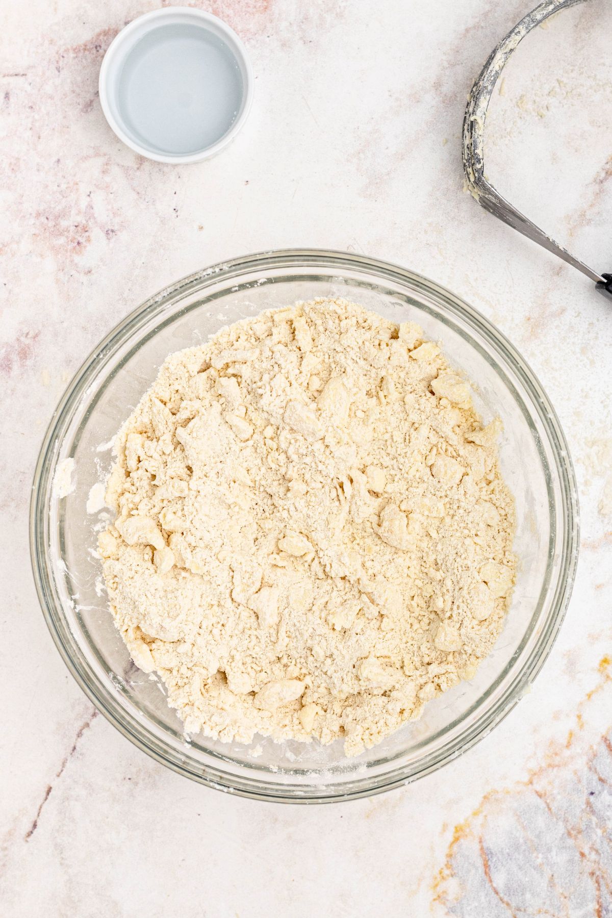 Butter, mixed with flour and other dry ingredients, in a clear glass bowl, before adding water, to make a homemade pie crust. 