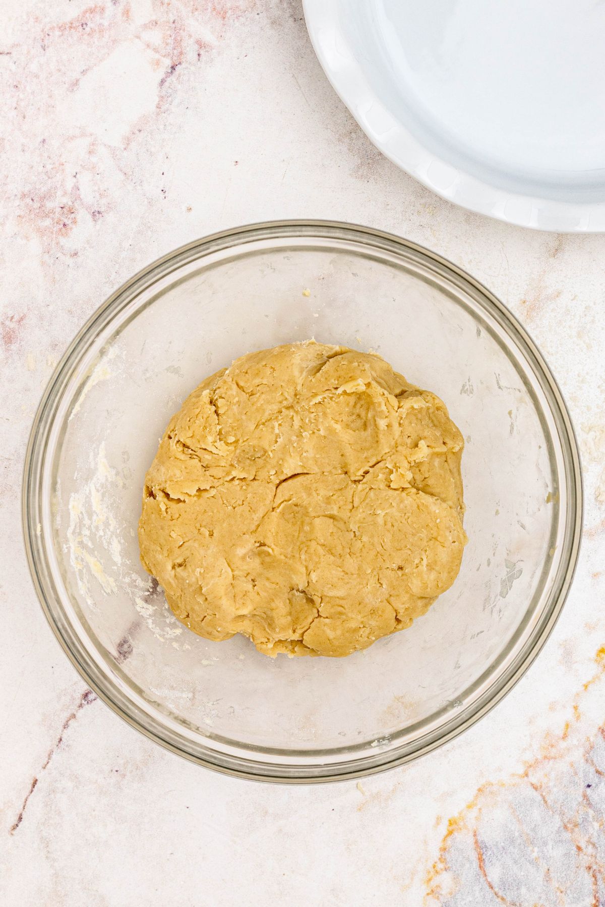 Ball of golden pie crust dough in a clear glass bowl. 
