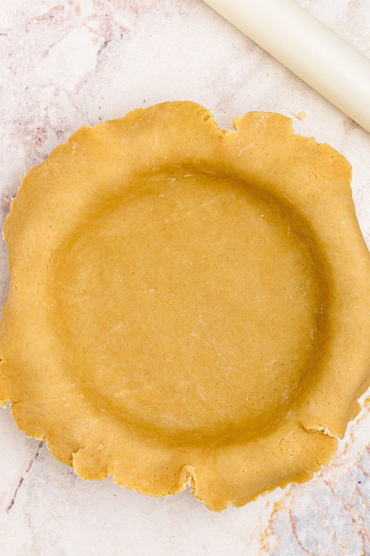 Golden pie crust rolled into pie plate, before trimming the edges. 