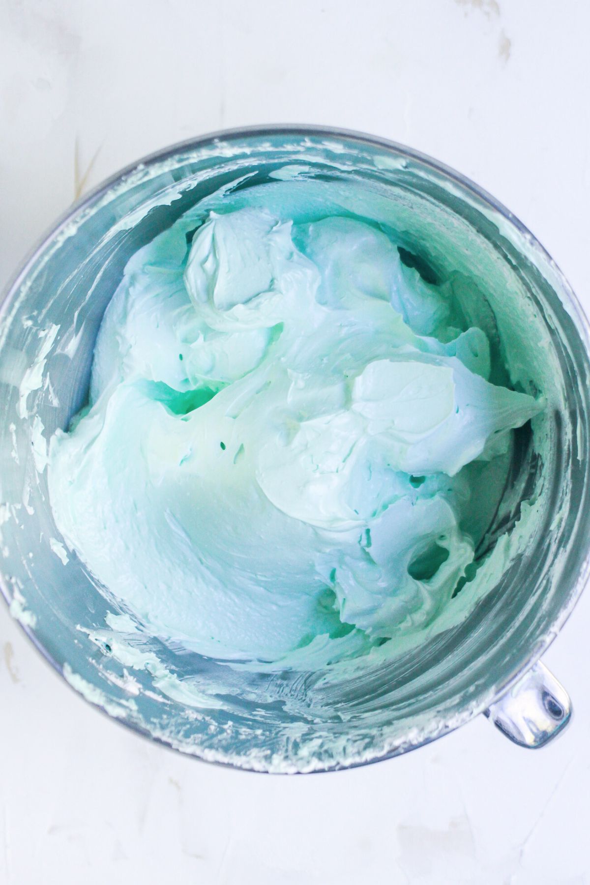 Green coloring and vanilla extract added to meringue in a silver bowl.