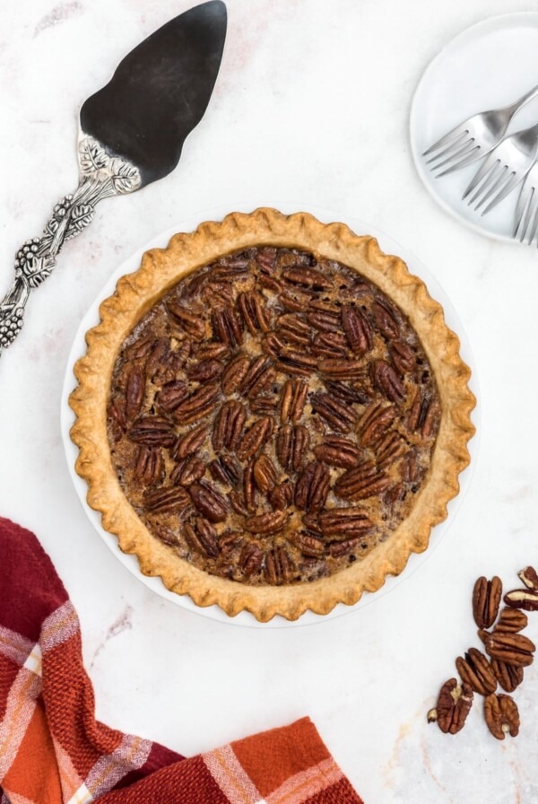 Pecan pie with golden fluted crust on a marble table with spatula and pecans on the table.