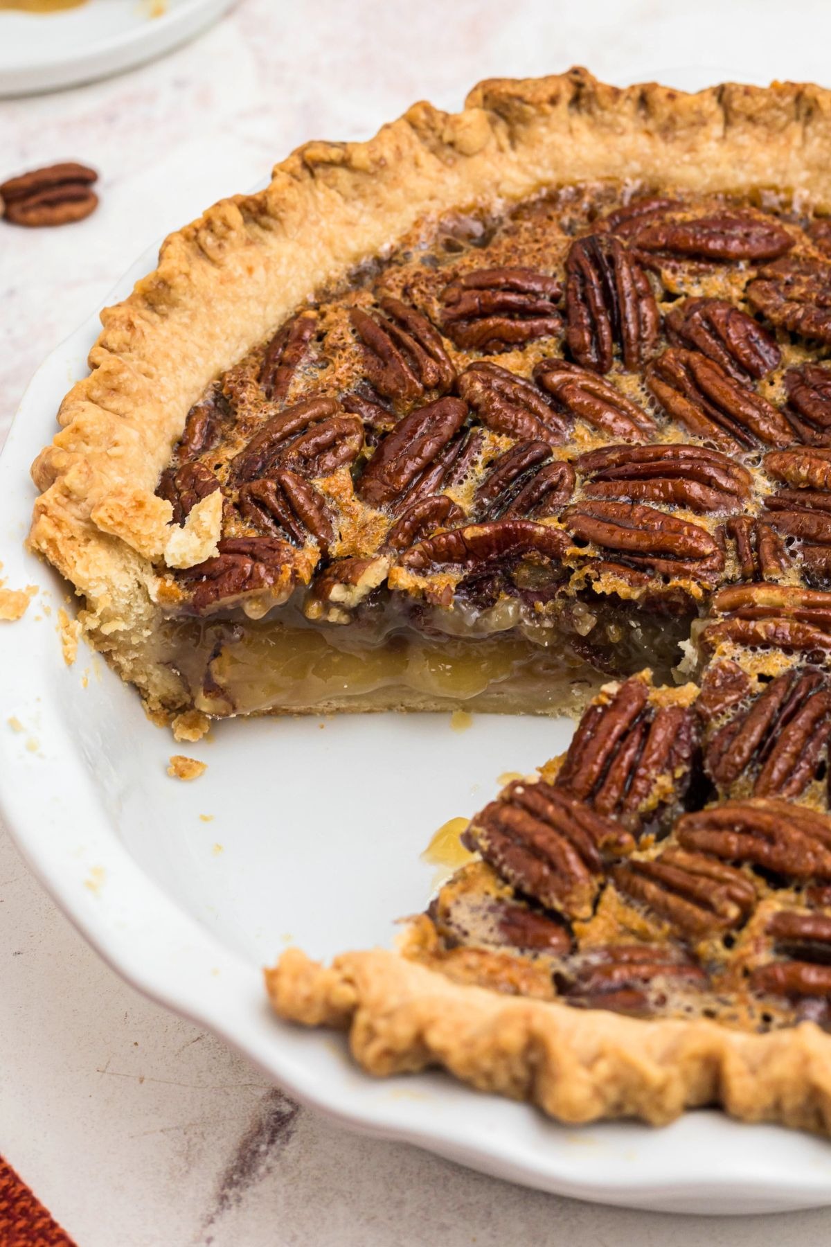Golden crusted pecan pie with creamy filling and a slice missing, in a white pie plate. 