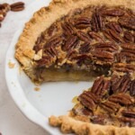 Golden crusted pecan pie with creamy filling and a slice missing, in a white pie plate.
