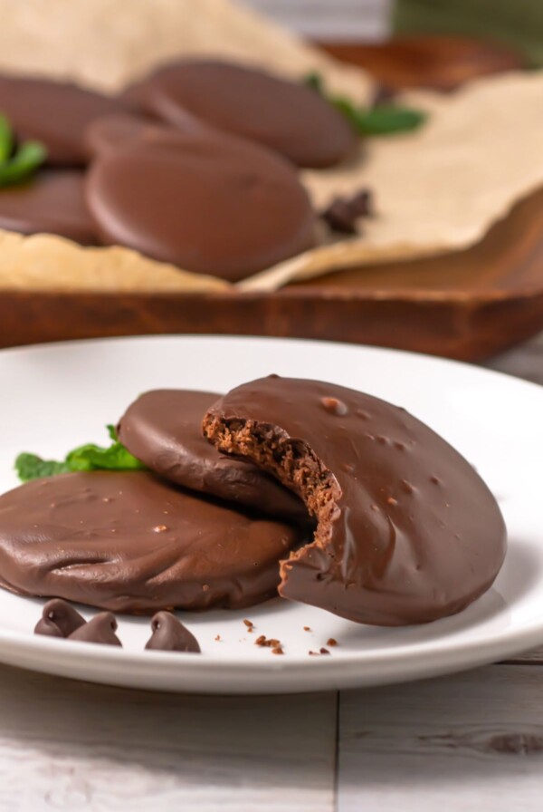Chocolate round cookies, dipped in cookies, on a small white plate with the top cookie missing a bite.