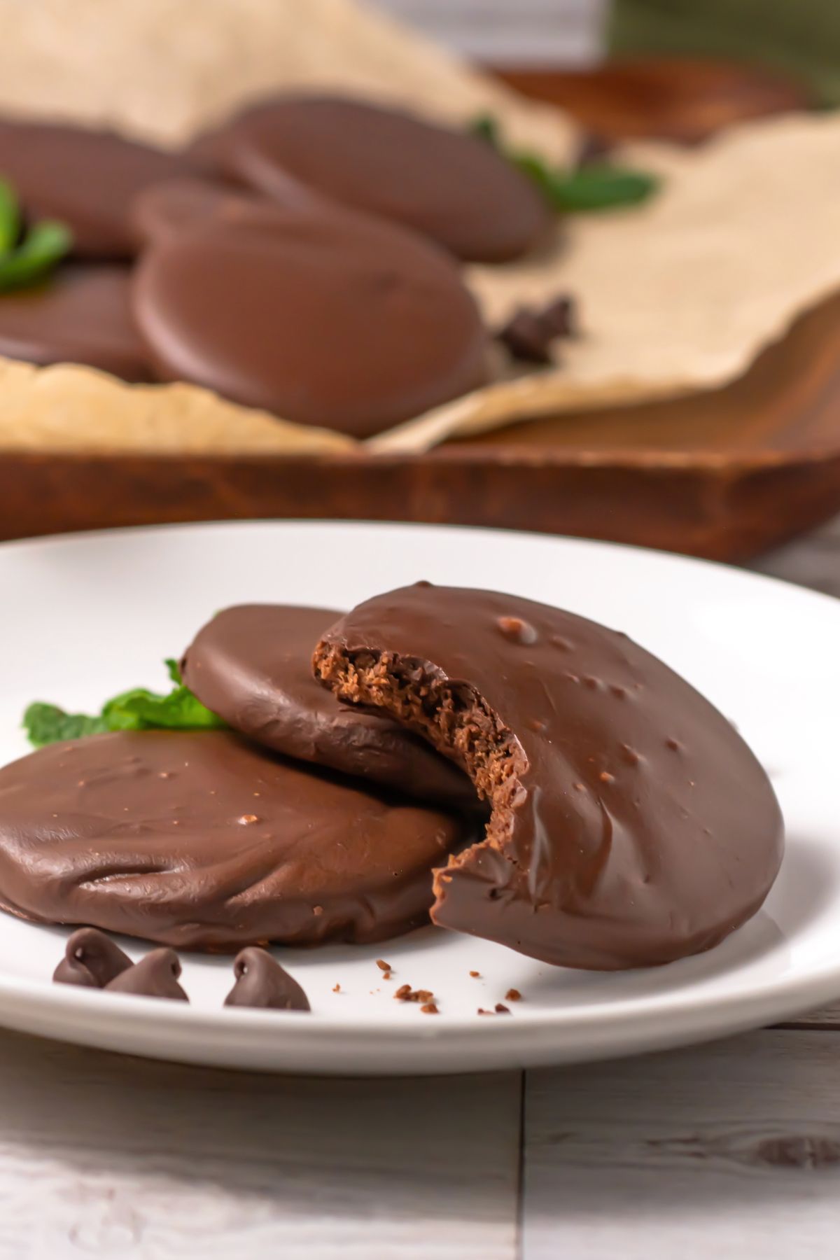 Chocolate round cookies, dipped in cookies, on a small white plate with the top cookie missing a bite.