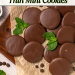Thin chocolate coated cookies, on brown parchment paper, with a few mint leaves on the paper with the cookies.