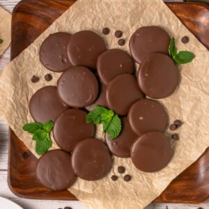 Thin chocolate coated cookies, on brown parchment paper, with a few mint leaves on the paper with the cookies.