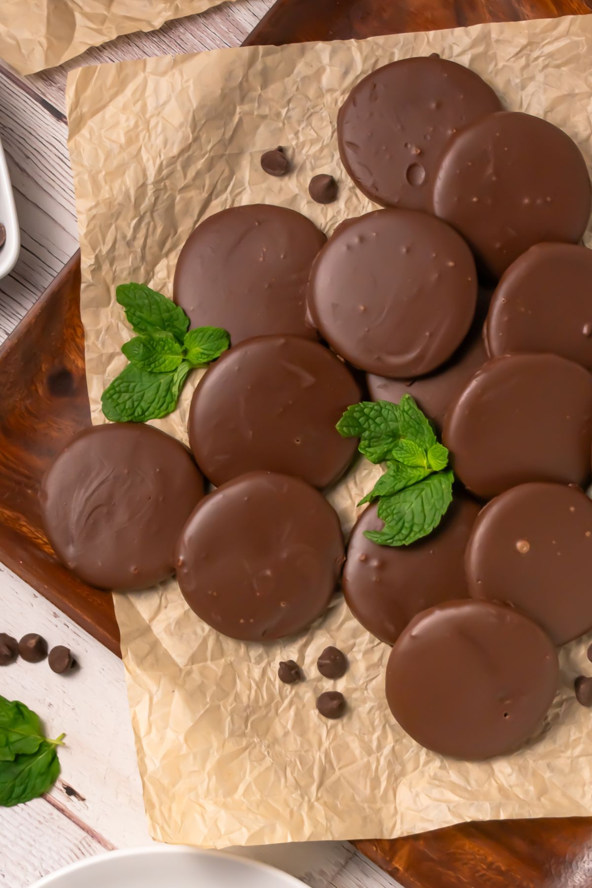 Thin chocolate coated cookies, on brown parchment paper, with a few mint leaves on the paper with the cookies.