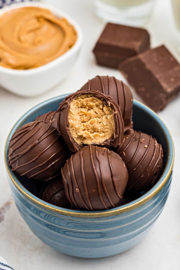 Chocolate covered peanut butter balls, stacked on a white plate, with the top piece missing a bite, next to a blue and white striped linen.