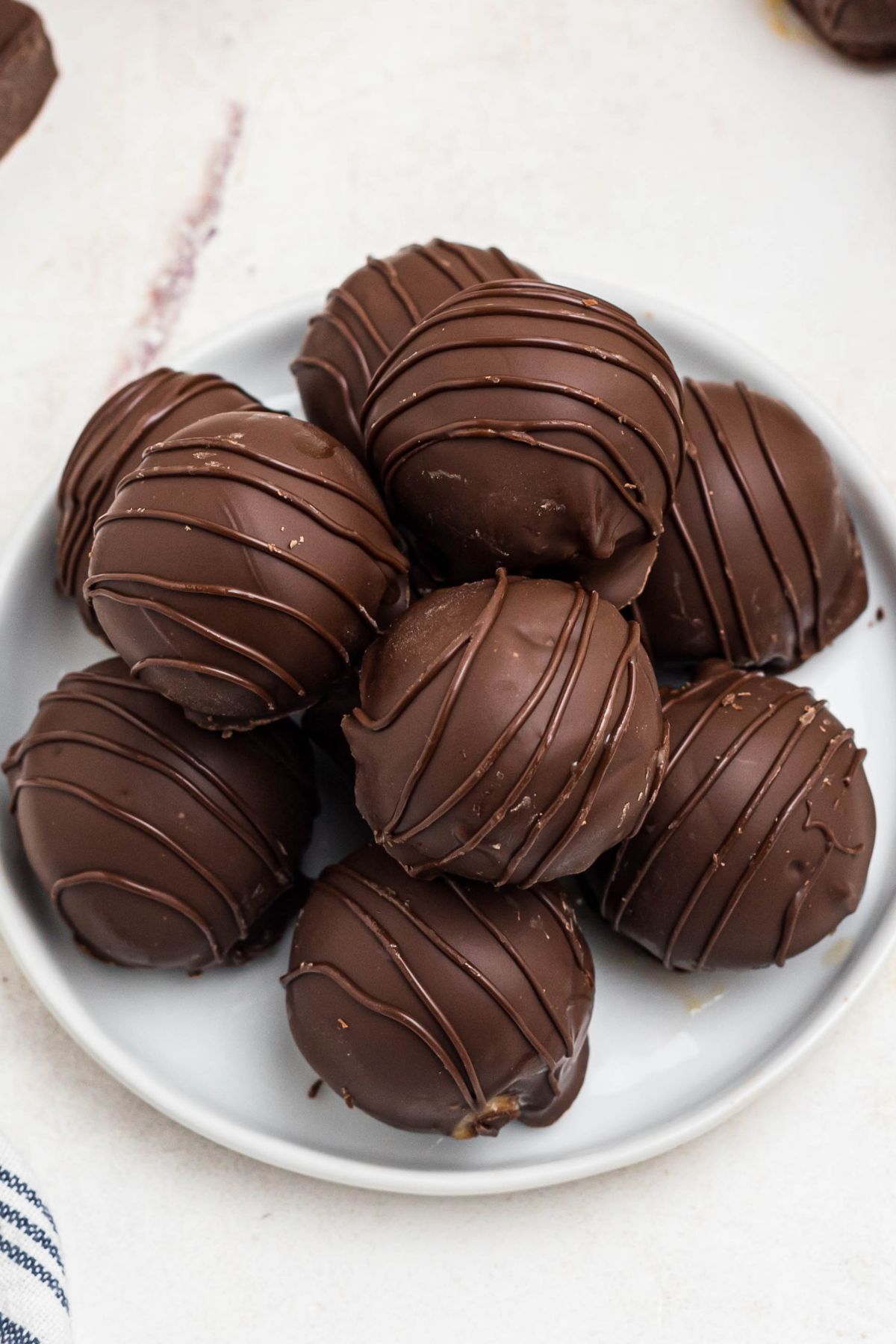 Chocolate coated peanut butter balls, drizzled with chocolate for decoration, on a white plate. 