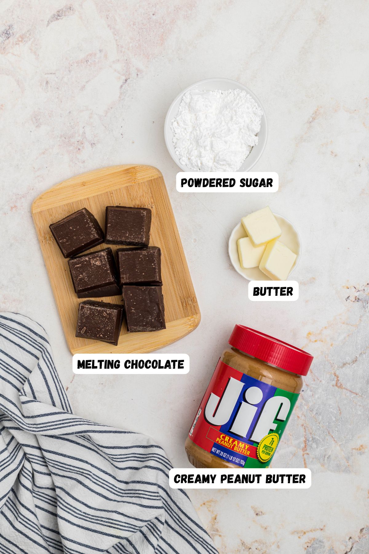 Peanut butter, chocolate, butter, and powdered sugar, on a white marble table, with labels next to each one. 
