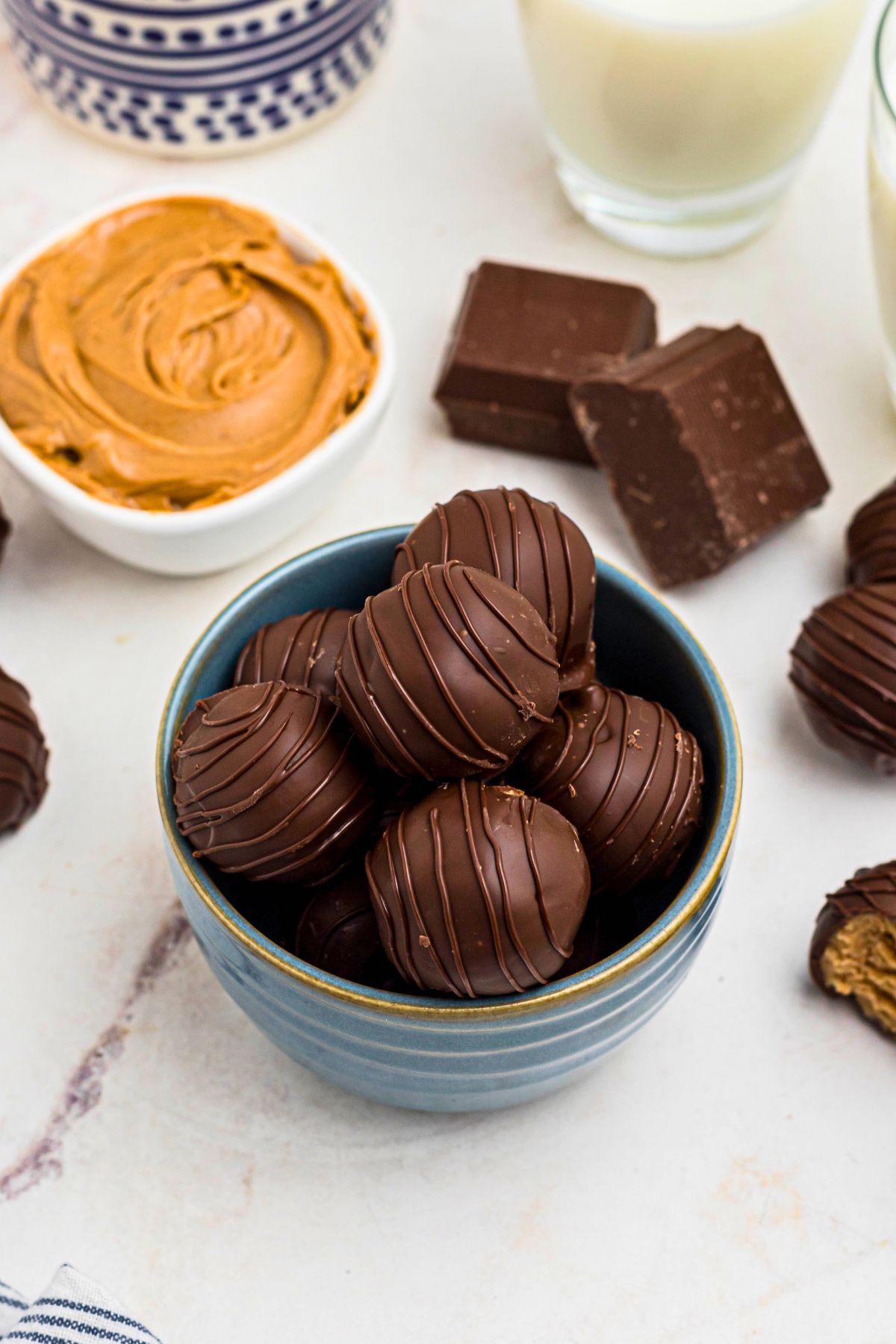 Chocolate covered peanut butter balls, stacked on a white plate, next to a blue and white striped linen.