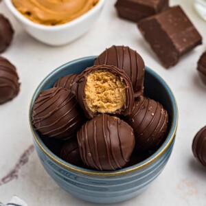 Chocolate covered peanut butter balls, stacked on a white plate, with the top piece missing a bite, next to a blue and white striped linen.