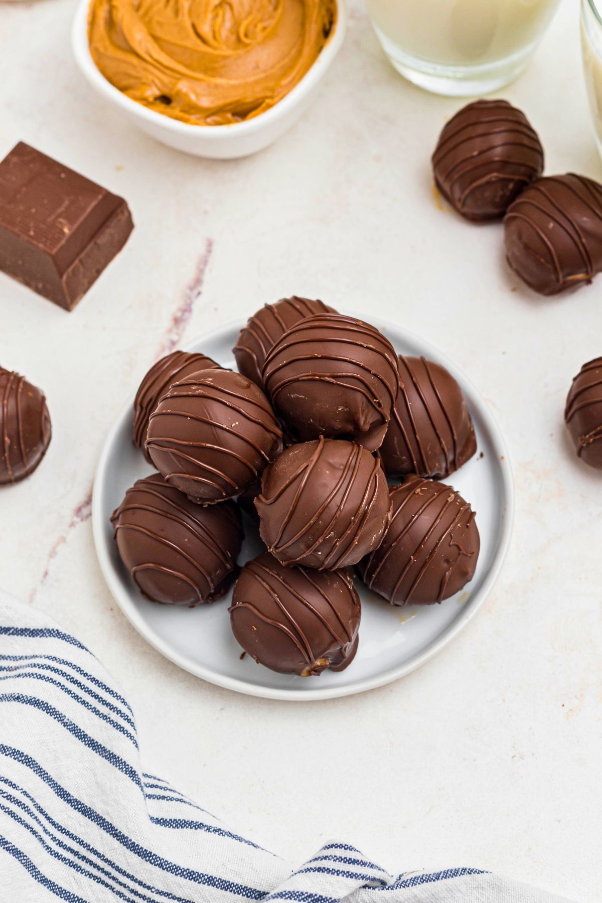 Chocolate covered peanut butter balls, stacked on a white plate, next to a blue and white striped linen. 