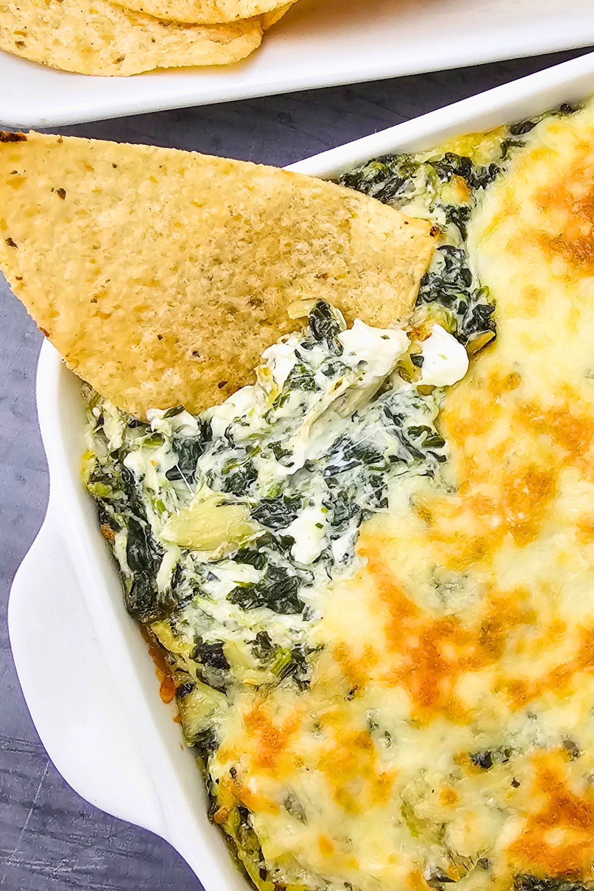 Creamy dip in a square dish with a tortilla chip dipping some out.