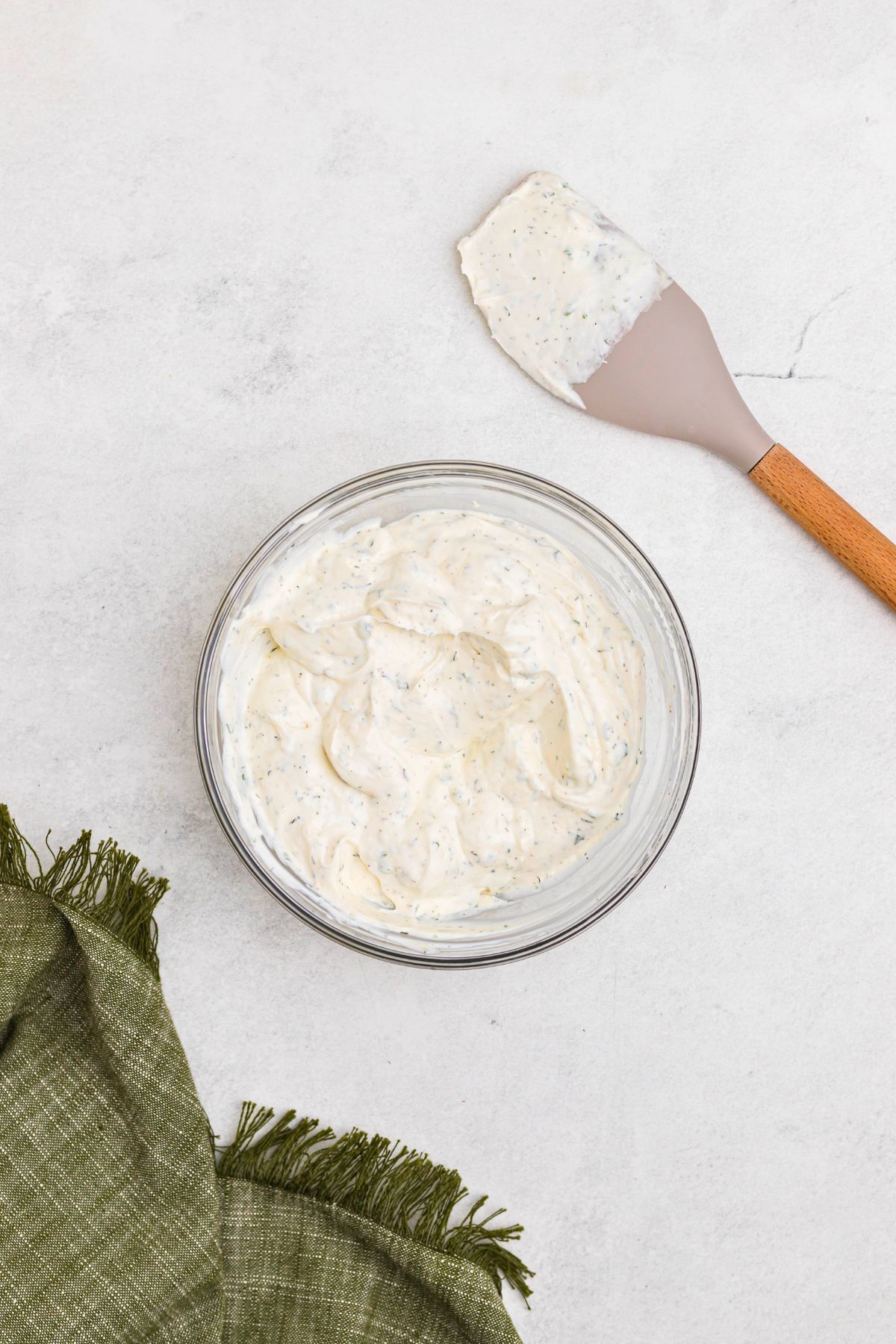 Herbs and spices mixed with sour cream and mayo, in a clear glass bowl until ingredients are well combined into a dip.