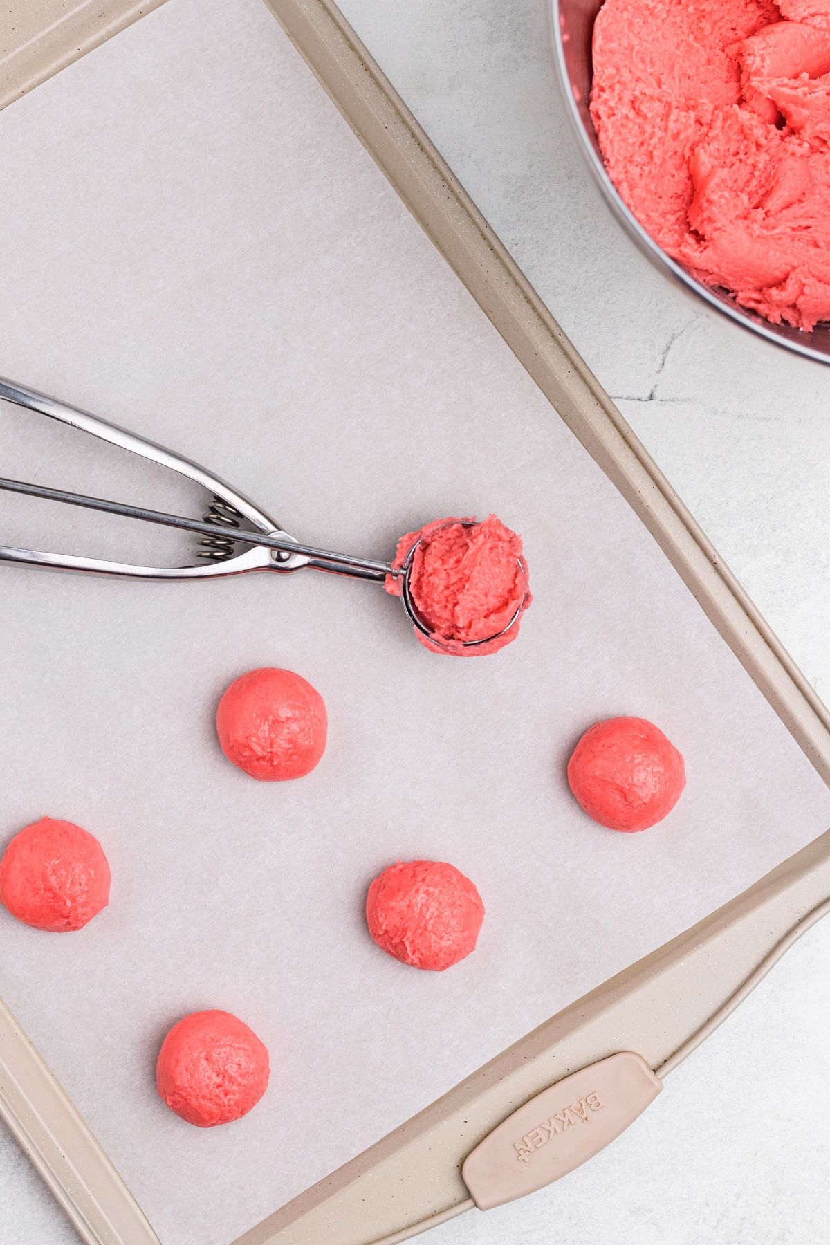 Raw pink strawberry cookie dough being scooped onto baking sheet lined with parchment paper.