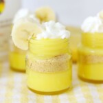 Bright yellow pudding layers in mini jars, topped with whipped cream and garnished with a banana slice.